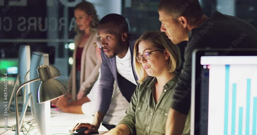 This office stays abuzz with productivity no matter the hour. Business group of diverse colleagues using computer and discussing work at a table during a late night in a modern office