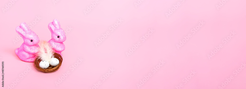 Easter bunnies and a nest with eggs on a pink background. Holiday concept. Closeup copy space