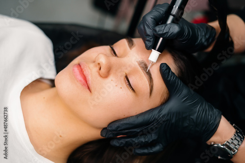 Beauty masters hands do permanent eyebrow makeup. Minimal trauma to skin. Eyebrow microblading is performed using manipulator handle and special nozzle with needles. Cosmetologist skill level photo