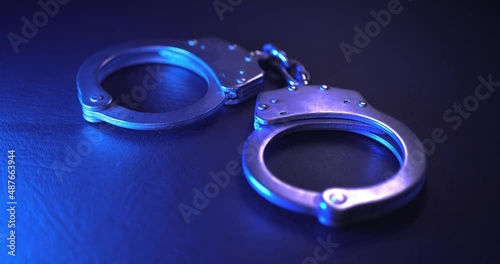 Pair of handcuffs used by law enforcement to arrest criminals, lit in red and blue flashing police lights. Justice or catching a guilty criminal concept.