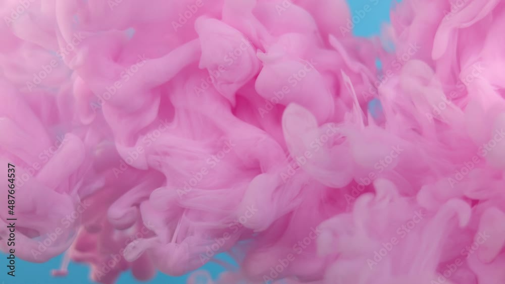 A pink cloud of colors slowly moving in the water on a blue background.