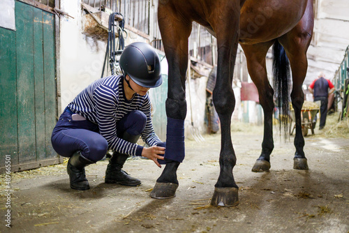 Canvas Print Young girl rider bandaging horse legs before training or competition