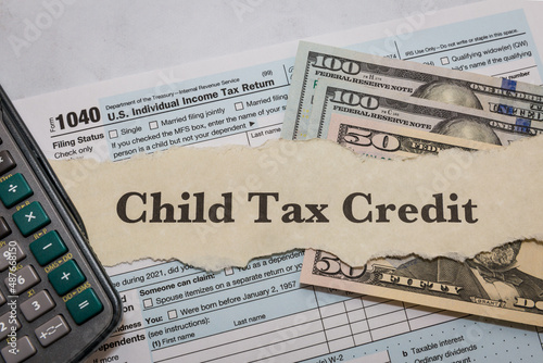 Child tax credit typed on paper with 1040 IRS form, calculator, and dollar bills