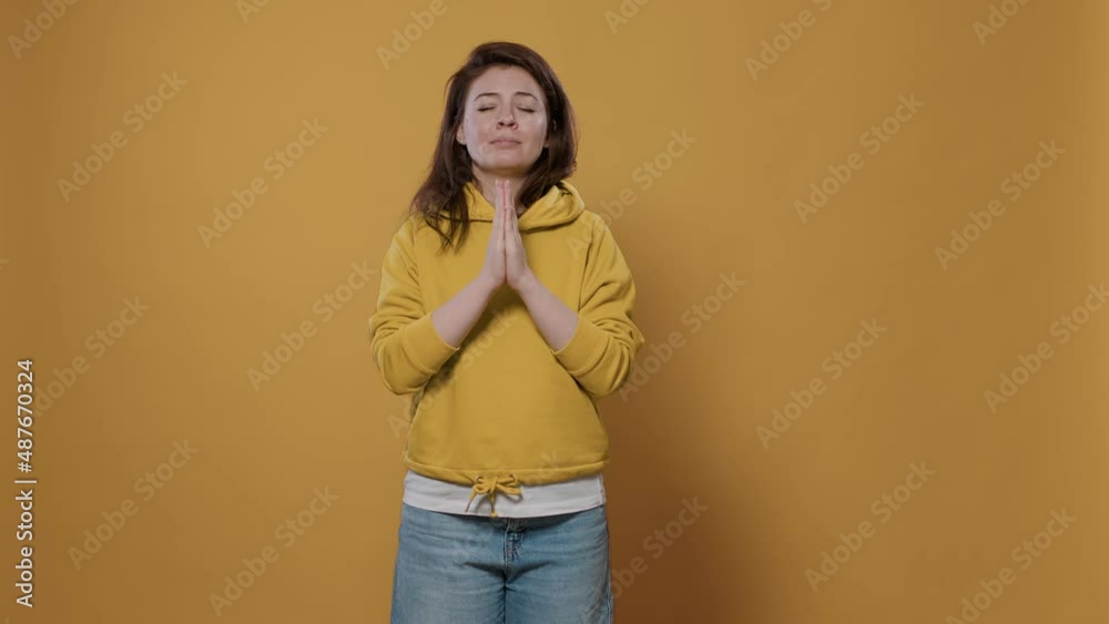 Humble young person wearing hoodie being religious having hope and faith with palms close together in studio. Casual woman feeling worried, looking up praying and asking for forgiveness. Humble young person wearing hoodie being religious having hope and faith with palms close together in studio. Casual woman feeling worried, looking up praying and asking for forgiveness.