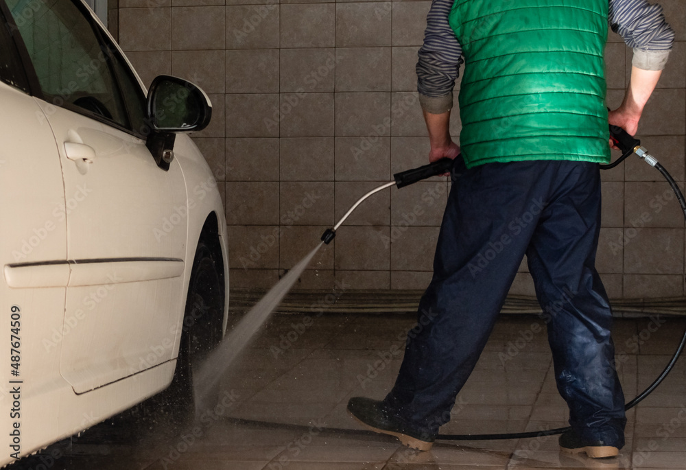 Fototapeta premium Guy washing white car with powerful water jet in open garage box