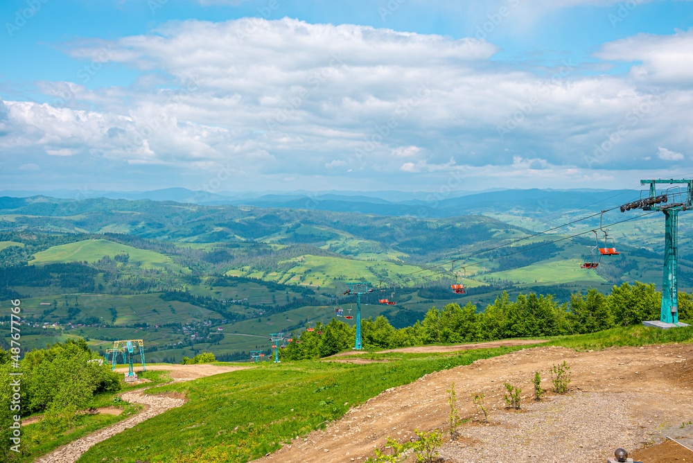 Fototapeta premium Winding dirtroad and ski lifts on grassy covered hill of countryside on summer day, Mountain road beside chair lifts with beautiful rural landscape