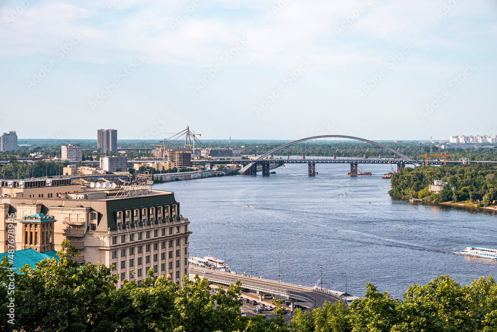 Kyiv, Ukraine. July 20, 2021. Beautiful cityscape with arched bridge and river dnieper and buildings on left of riverbank