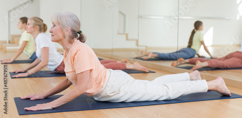 Elderly woman lying in cobra pose while training yoga with her family in studio.