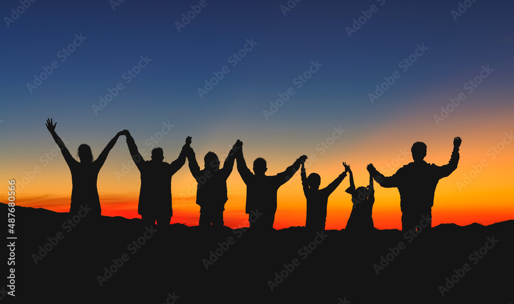 People group standing with raised hands on the mountain at the sunset sky.Silhouette People group standing with raised hands on the mountain at the sunset sky.Silhouette