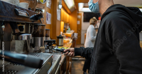 Young guy with a mask making a coffee in a bar machine