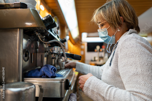 Old woman with a mask making a coffee in a bar machine