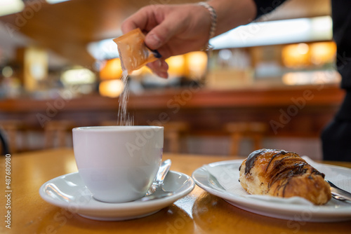 Hand putting sugar in coffee next to a chocolate croissant in a bar
