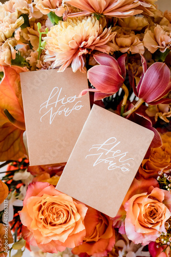 фотографія His and Hers vow books resting on colorful wedding flowers