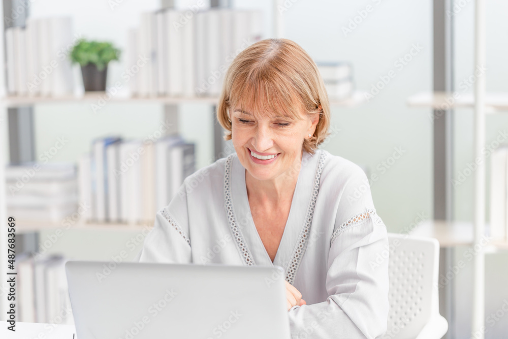 Portrait of cheerful woman using laptop and smartphone at home, Mature woman in living room with laptop talking video call on modern computer gadget Portrait of cheerful woman using laptop and smartphone at home, Mature woman in living room with laptop talking video call on modern computer gadget