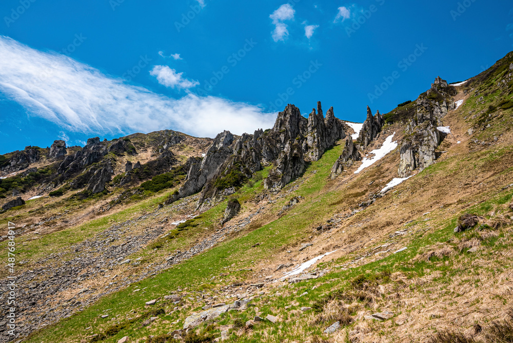Rocky cliff and peak of mountain with steep slope and moss against cloudy sky. Scenic view of cliff and sky