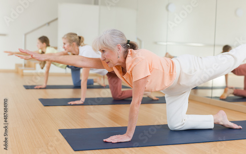 Active senior woman exercising stretching workout and incline during yoga class in fitness studio photo