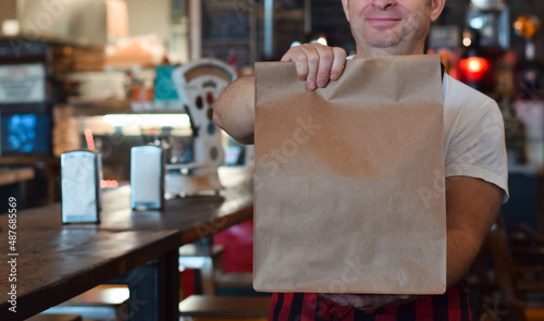 Restaurant employee holding paper take out bag with customer food order