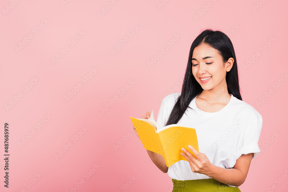 Portrait of beautiful Asian young woman teenage smiling holding a yellow book and reading, studio shot isolated on pink background with copy space Portrait of beautiful Asian young woman teenage smiling holding a yellow book and reading, studio shot isolated on pink background with copy space