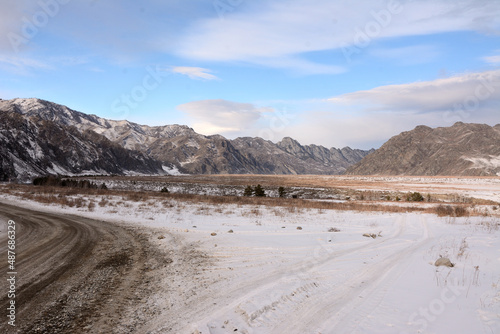 A fork in the field roads in the snow-covered steppe of a beautiful valley surrounded by winter mountains.