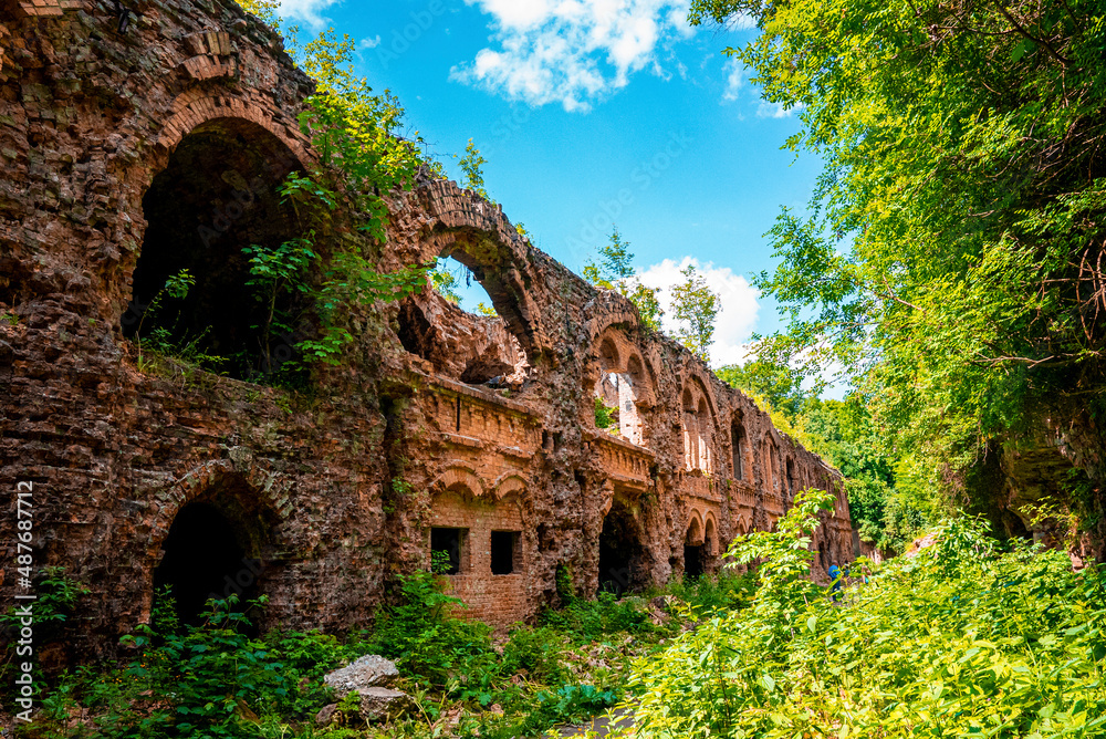 Ruins of abandoned old fortification fort surrounded by green plants on sunny day, Remains of ancient old castle against sky