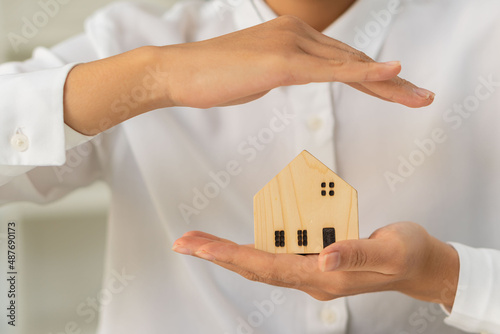 Asian woman's hand holds a small house model and folds her arms in defense above insurance concept. real estate and foster home care and family concepts.