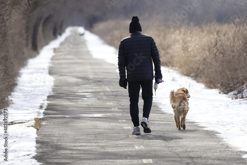 A lone, older male makes way down a long nature trail on an overcast day accompanied by his faithful dog.