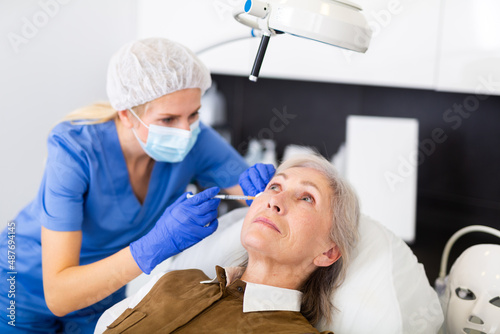 Closeup portrait of aged woman getting injections for face skin tightening at aesthetic cosmetology clinic ..