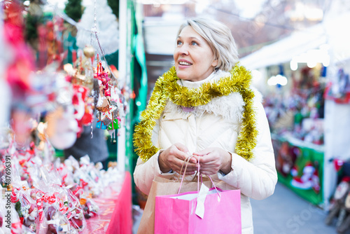 Mature woman choosing decorations at Christmas market and walking