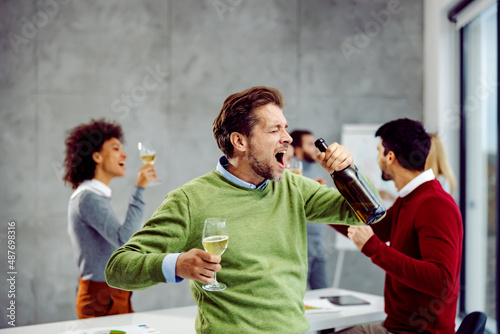 Canvas Print Businessman celebrating success at work with bottle of champagne.