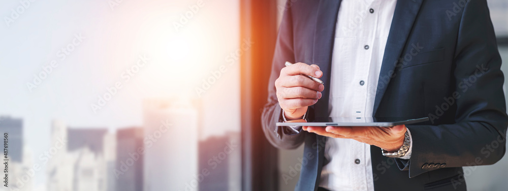 Thoughtful businessman in suit holding digital tablet while standing near the window in modern office. Thinking and planning business strategy, financial and marketing analysis. - obrazy, fototapety, plakaty 