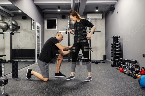 Tableau sur toile An instructor helps a woman standing to train a suit for EMS technology in a gym