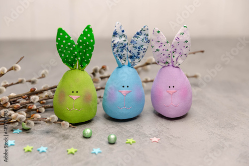 Smart Easter composition is made of multicoloured cute handmade textile Easter rabbits. A bunch of willow branches. Easter decoration on the light grey concrete background with copyspace.