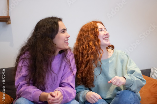 Happy teenagers sitting on sofa at home and looking away. Medium shot of smiling girls spending time with friends on weekend, laughing and talking. Emotion, entertainment concept