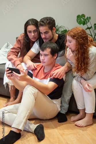 Friends sitting on sofa and watching sports game on phone. Vertical shot of excited men and women cheering for team at tense moment, supporting football team. Friendship, entertainment concept