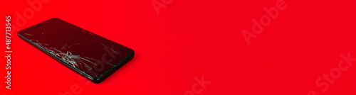A mobile phone with a broken screen lies on a red background. A broken smartphone. Electronic gadget in need of repair. Horizontal image. Banner for insertion into site.