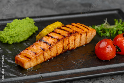 grilled salmon fillet on a black plate with tomatoes on a gray background macro photo
