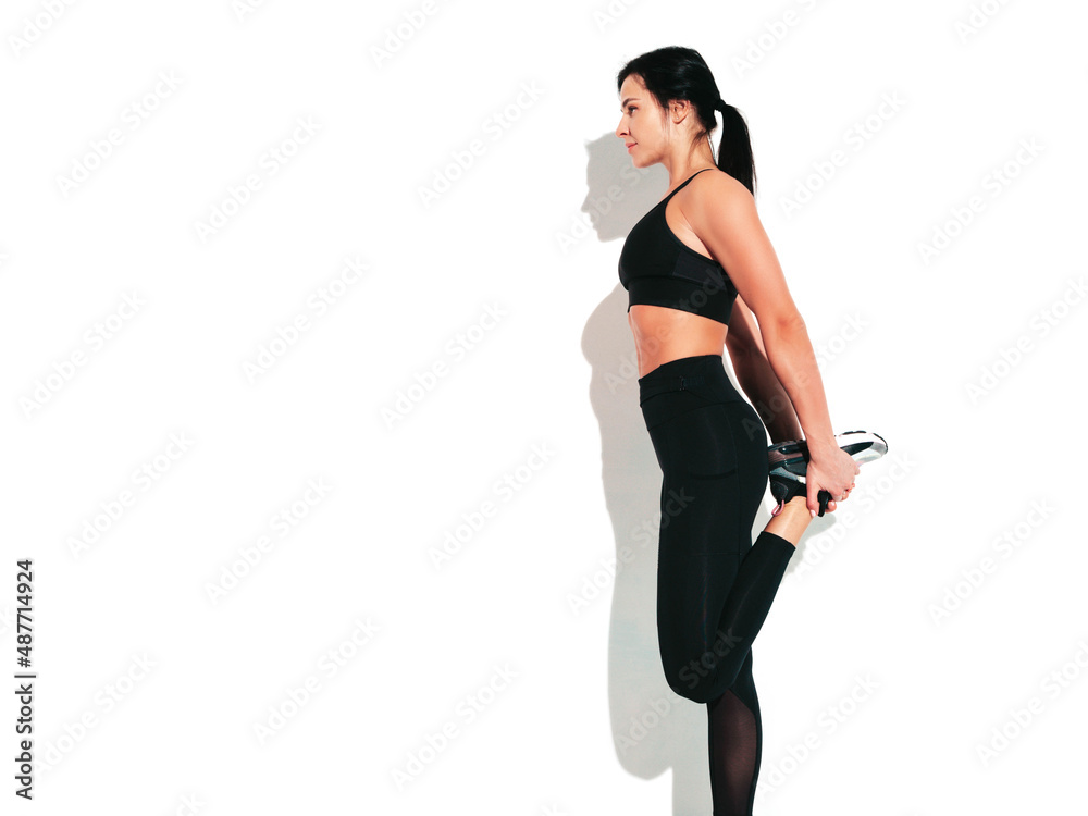Portrait of fitness confident woman in black sports clothing. Sexy young beautiful model with perfect body. Female isolated on white wall in studio. Stretching out before training Portrait of fitness confident woman in black sports clothing. Sexy young beautiful model with perfect body. Female isolated on white wall in studio. Stretching out before training