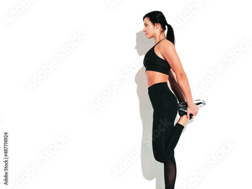 Portrait of fitness confident woman in black sports clothing. Sexy young beautiful model with perfect body. Female isolated on white wall in studio. Stretching out before training
