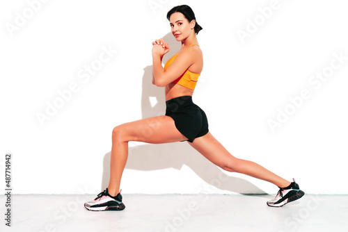 Portrait of fitness confident woman in black sports clothing. Sexy young beautiful model with perfect body. Female isolated on white wall in studio. Stretching out before training. Doing lunges
