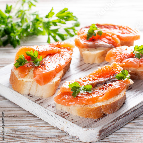 Slices of fresh baguette with butter and salmon served on wooden board on wood table