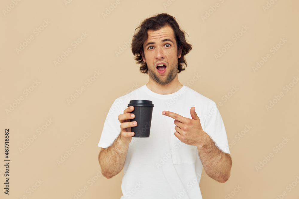 Attractive man in a white T-shirt with a black glass in hand Lifestyle unaltered Attractive man in a white T-shirt with a black glass in hand Lifestyle unaltered