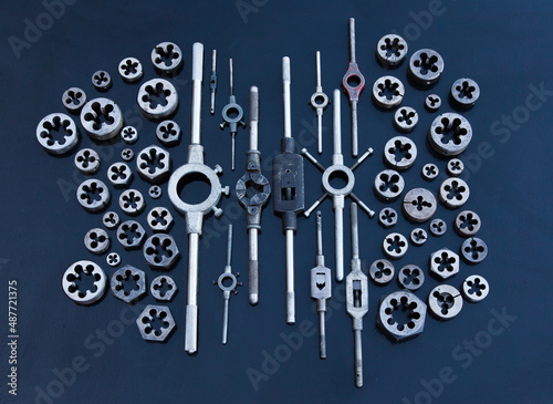 A lot of dies and holders for them of different sizes for threading in metal, on a black background.