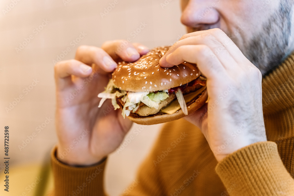 A man eats a burger with meat in a cafe. Fast food, junk food, fast carbs, obesity, overeating, stress concept. A man eats a burger with meat in a cafe. Fast food, junk food, fast carbs, obesity, overeating, stress concept.