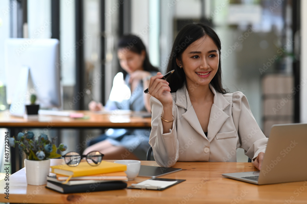 Happy asian woman worker sitting at her workplace and using computer laptop. Happy asian woman worker sitting at her workplace and using computer laptop.