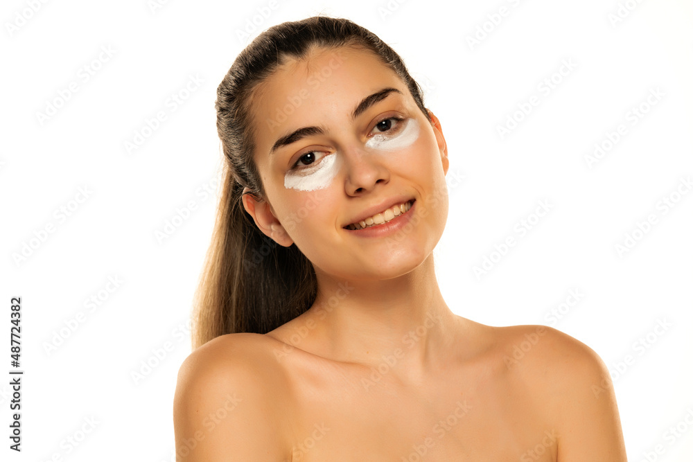 Portrait of a young happy woman with cosmetic product under her eyes