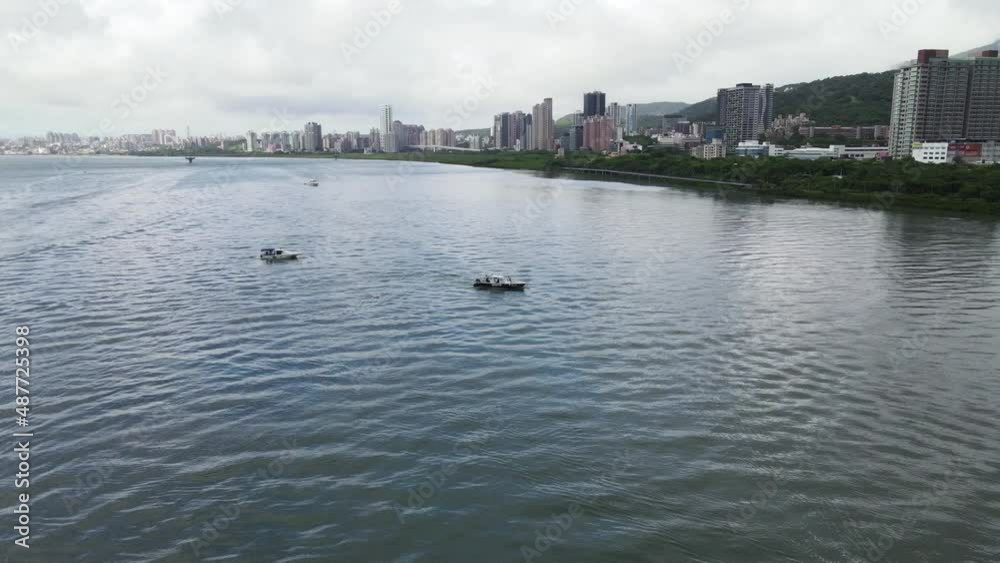 Fishing boats drifting in river with buildings lining riverside on cloudy day Fishing boats drifting in river with buildings lining riverside on cloudy day