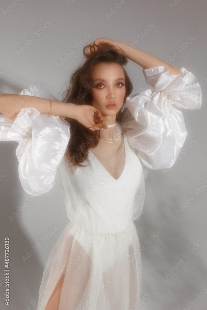 Stunning young woman with trendy makeup wearing modish white dress at the studio background Stunning young woman with trendy makeup wearing modish white dress at the studio background