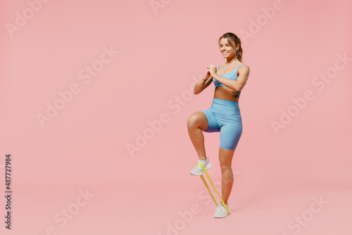 Full body young smiling sporty athletic fitness trainer instructor woman wear blue tracksuit spend time in home gym use fitness rubber bands isolated on plain pink background. Workout sport concept.