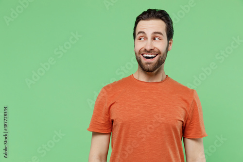 Young surprised amazed man 20s in casual orange t-shirt look aside on workspace area mock up copy space isolated on plain pastel light green color background studio portrait. People lifestyle concept.