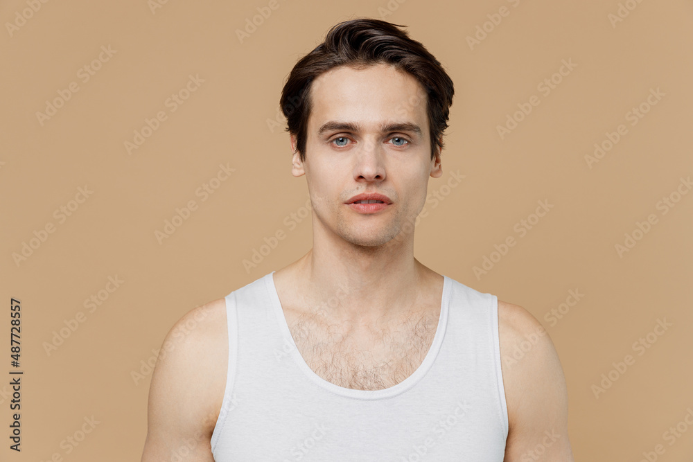 Attractive handsome good looking serious young man 20s perfect skin wearing undershirt look camera isolated on pastel pastel beige background studio Skin care healthcare cosmetic procedures concept. Attractive handsome good looking serious young man 20s perfect skin wearing undershirt look camera isolated on pastel pastel beige background studio Skin care healthcare cosmetic procedures concept.
